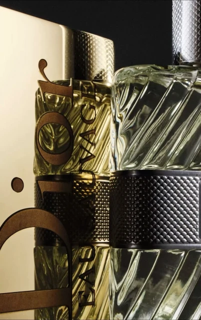 Multiple textured glass and gold bottles of perfume stacked on top of each other in a studio setting, illuminated with dramatic lighting.