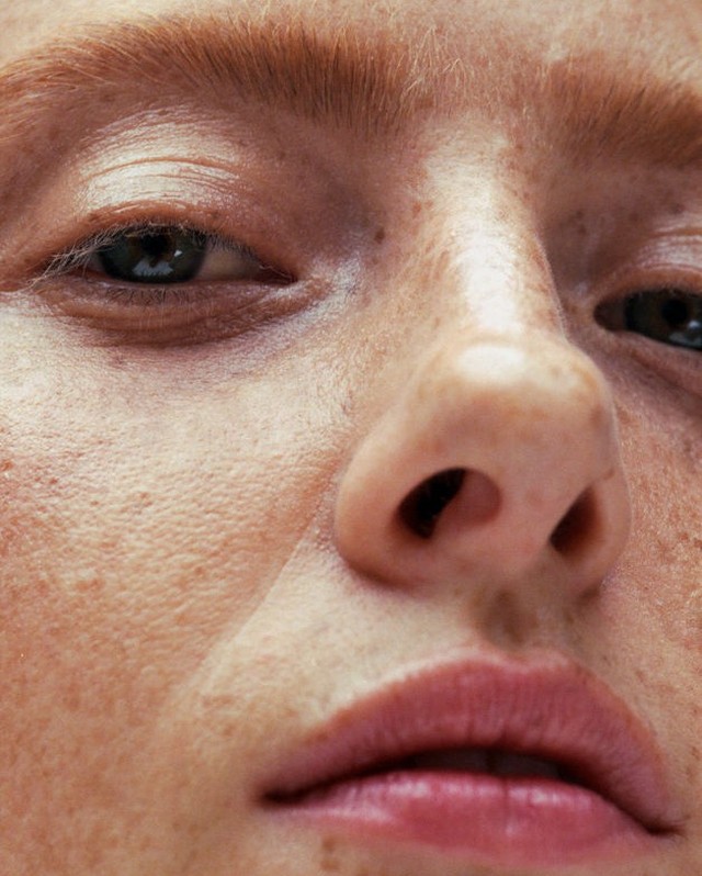 Close-up portrait of a fair-skinned woman's face, freckles, and light red hair, with a focus on her eyes, nose, and lips.