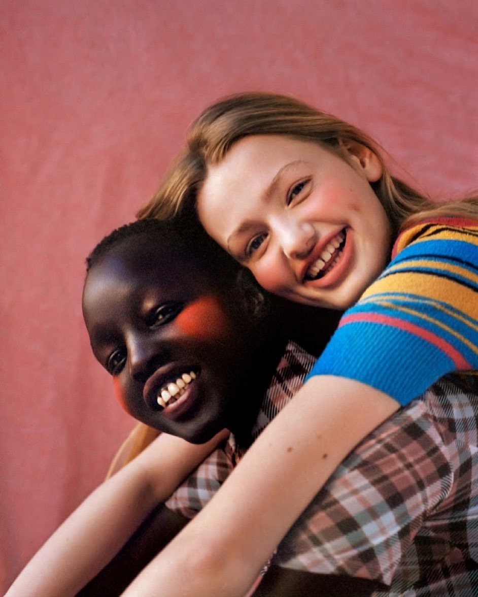 Two young female models smiling warmly while embracing against a textured pink background