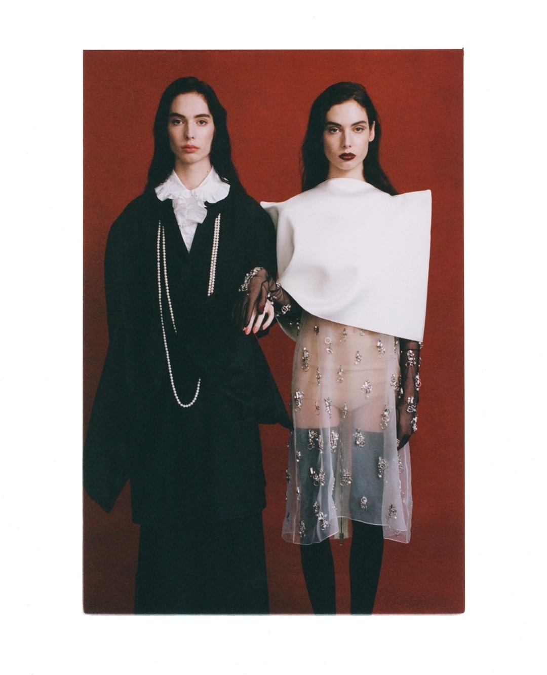 Two fashion models in contrasting black and white outfits pose against a red backdrop, showcasing modern and elegant clothing styles.