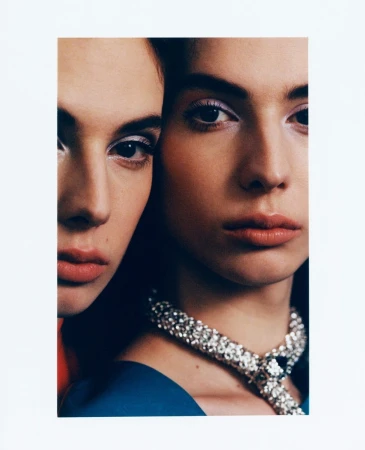 Close-up studio shot of two female fashion models with neutral expressions, wearing blue tops and rhinestone necklaces against a white backdrop.