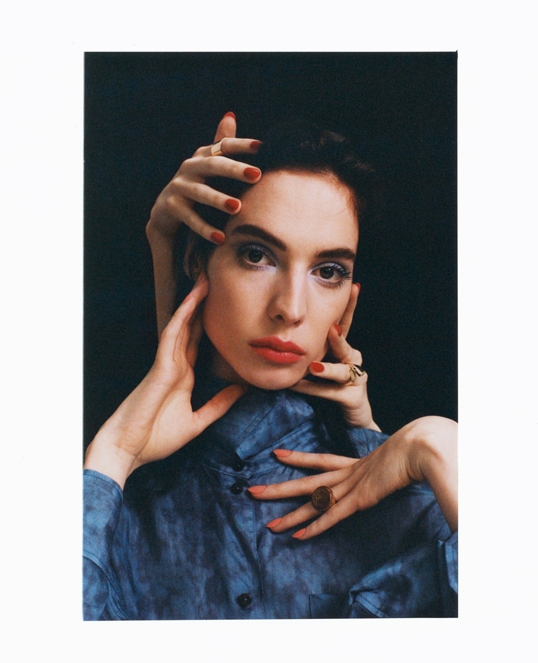 A woman poses in a photo studio with bright makeup and nail polish, surrounded by a second set of hands in a surreal composition.