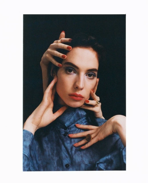 A woman poses in a photo studio with bright makeup and nail polish, surrounded by a second set of hands in a surreal composition.