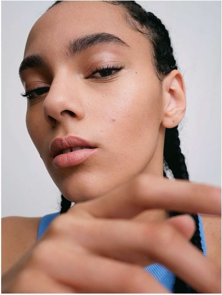 Close-up shot of a young adult female with light skin and braided hair. She is wearing a blue top against a plain white background.