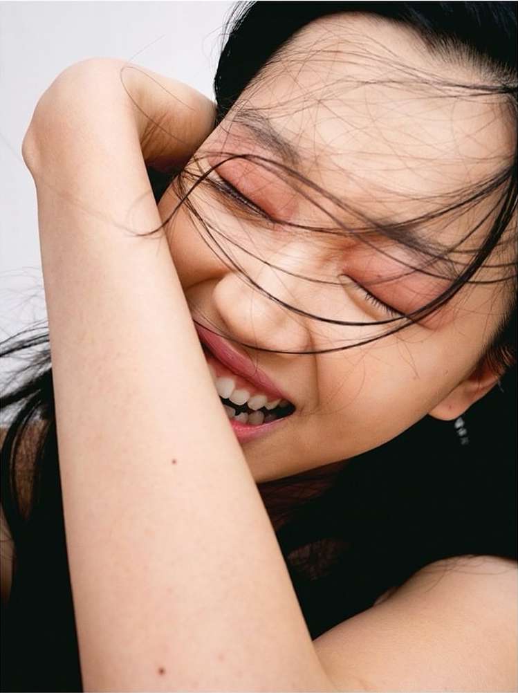 Close-up portrait of a laughing young woman with dark hair strands across her face, captured by photographer Benjamin Madgwick.