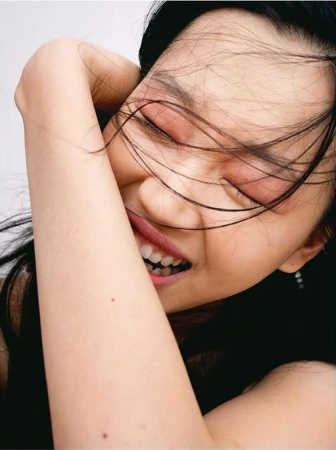 Close-up portrait of a laughing young woman with dark hair strands across her face, captured by photographer Benjamin Madgwick.