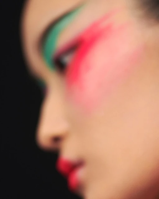 Extreme close-up of a female face with bold red lipstick and colorful green and red eye makeup against a dark background.