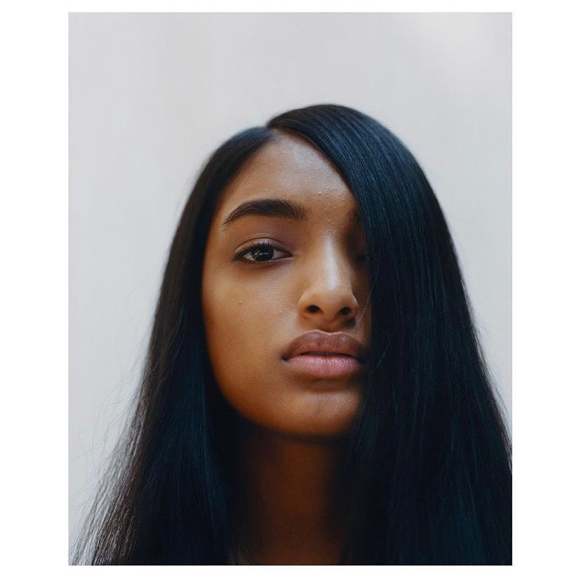 Close-up portrait of an adult female with dark skin and long dark hair in a studio setting with a neutral background.