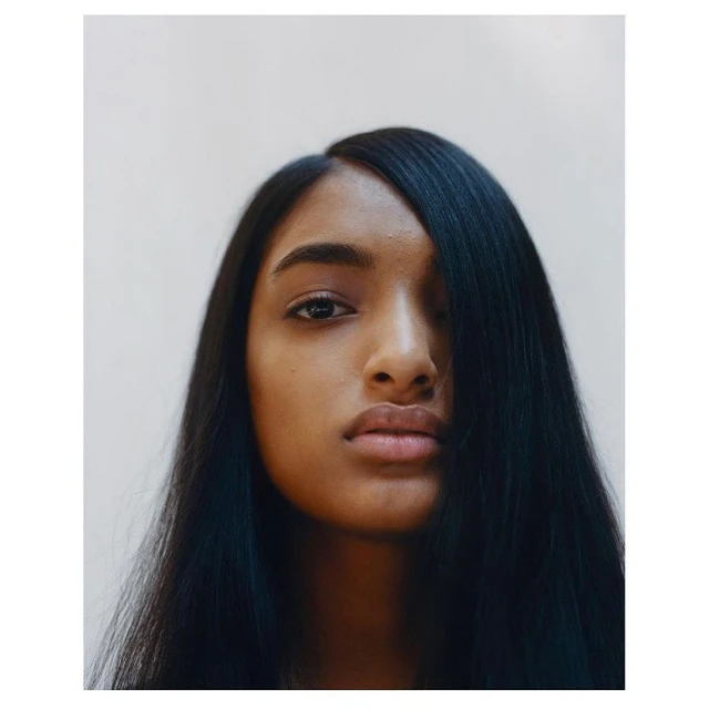 Close-up portrait of an adult female with dark skin and long dark hair in a studio setting with a neutral background.