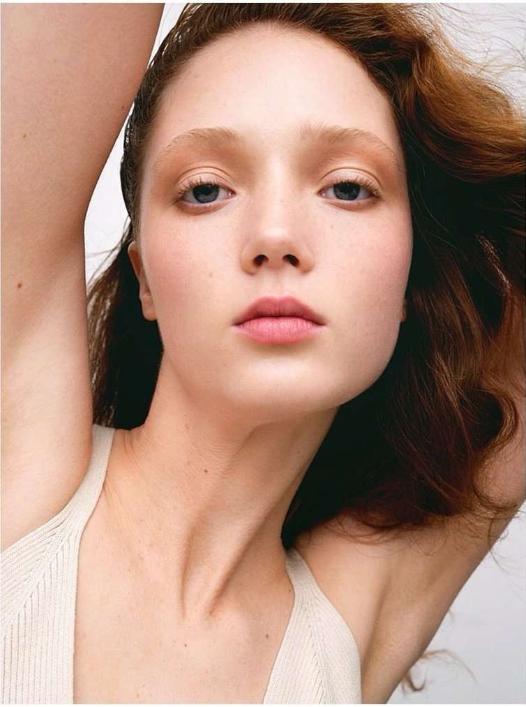 Close up portrait of a red haired woman with arms raised against a plain white background