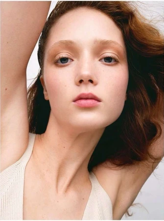 Close up portrait of a red haired woman with arms raised against a plain white background