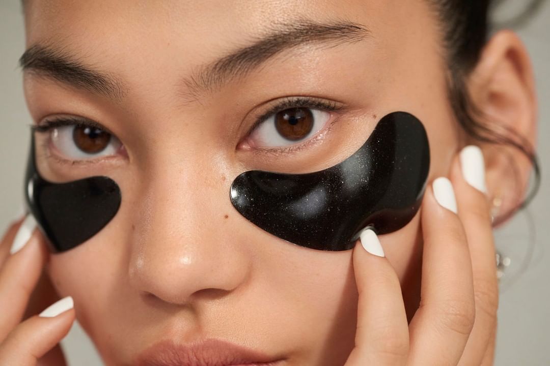 Close-up of a woman applying black under-eye patches, showcasing skincare and beauty treatment for reducing dark circles and puffiness.