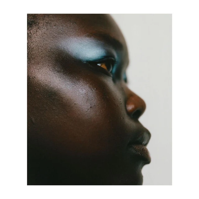 Close-up portrait of a beautiful dark-skinned woman with teal eyeshadow against a clean white background in a beauty editorial shot.