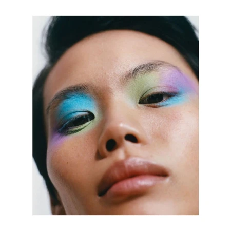 Close-up studio shot of an adult female with colorful pastel blue, green, and purple eyeshadow, fair skin and black hair.
