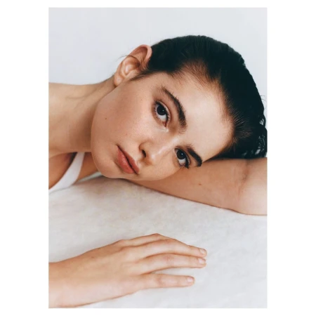 Close-up portrait of a woman with dark hair resting her head on her arm against a white background