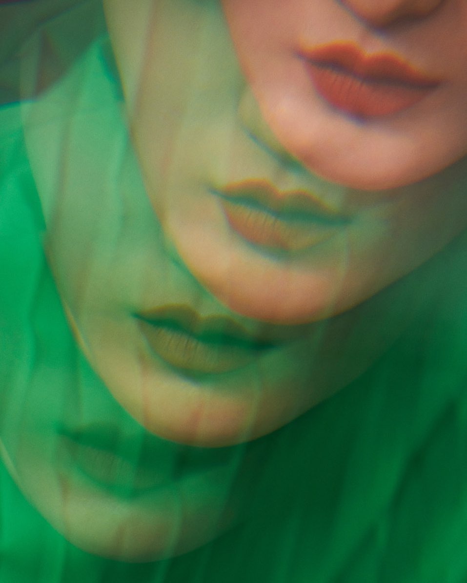 Abstract close-up of a person's face, featuring multiple exposures of the mouth and chin in shades of green and red.