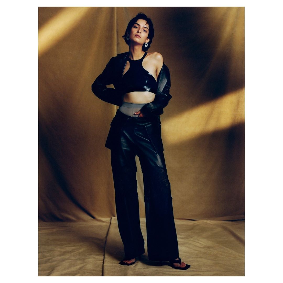 Woman in black leather jacket and matching trousers posing against a warm textured backdrop
