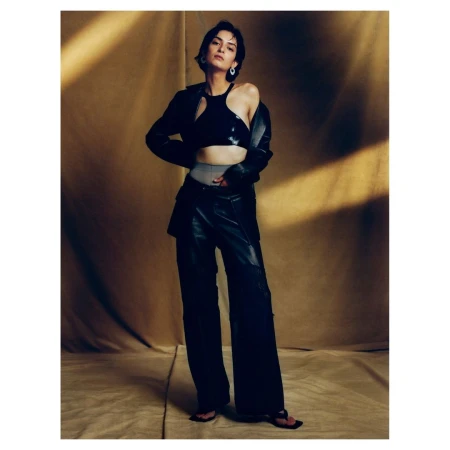 Woman in black leather jacket and matching trousers posing against a warm textured backdrop