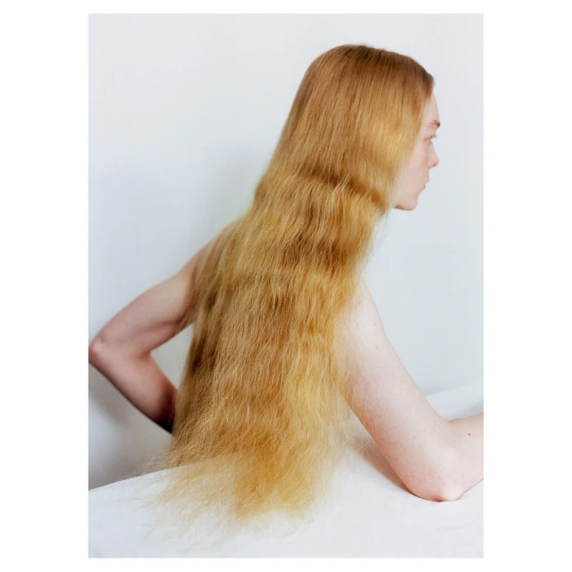 Portrait of a young woman with long, golden hair cascading over her shoulders, captured in a studio setting with a white background.