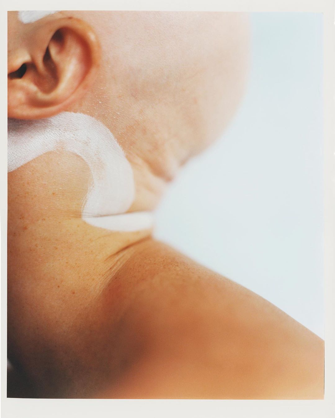 Close-up of a fair-skinned person's neck and upper shoulder with a white cream product applied, set against a pale background.