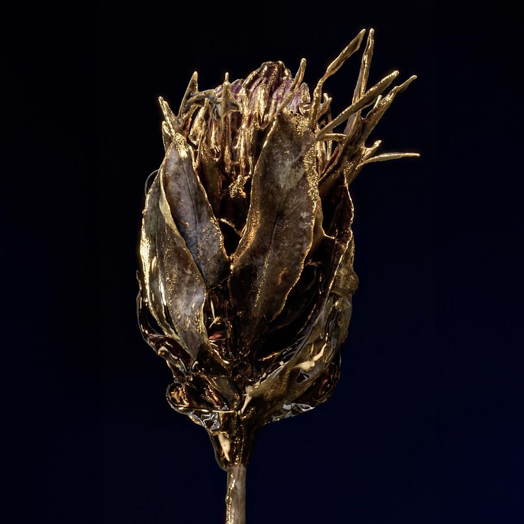 Close-up studio shot of a gold-colored flower bud sculpture on a stem against a dark background; metallic sheen and artistic form.