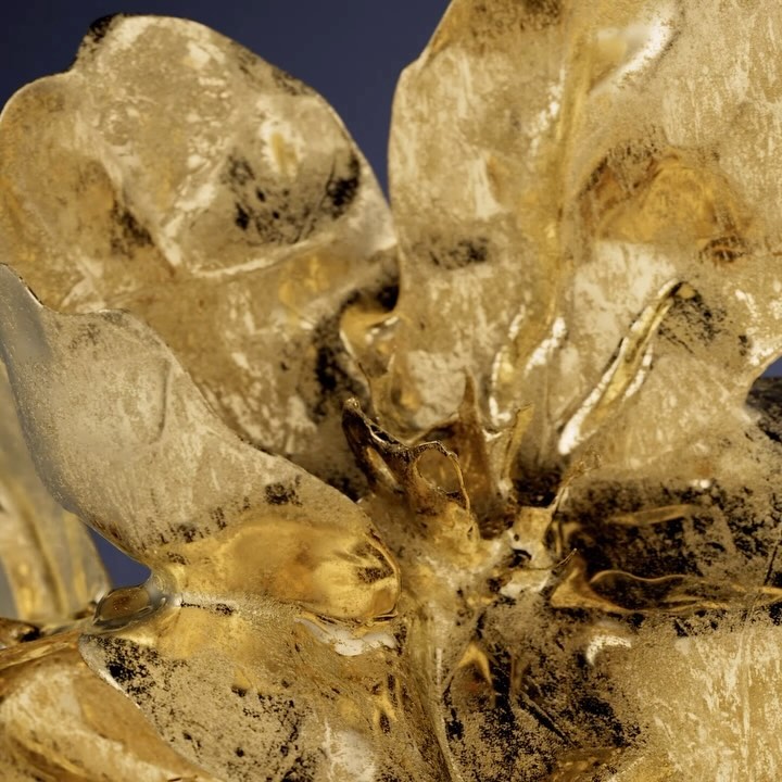 Close-up of a golden flower sculpture, showcasing intricate details and textures against a dark blue background, highlighting metallic luster.