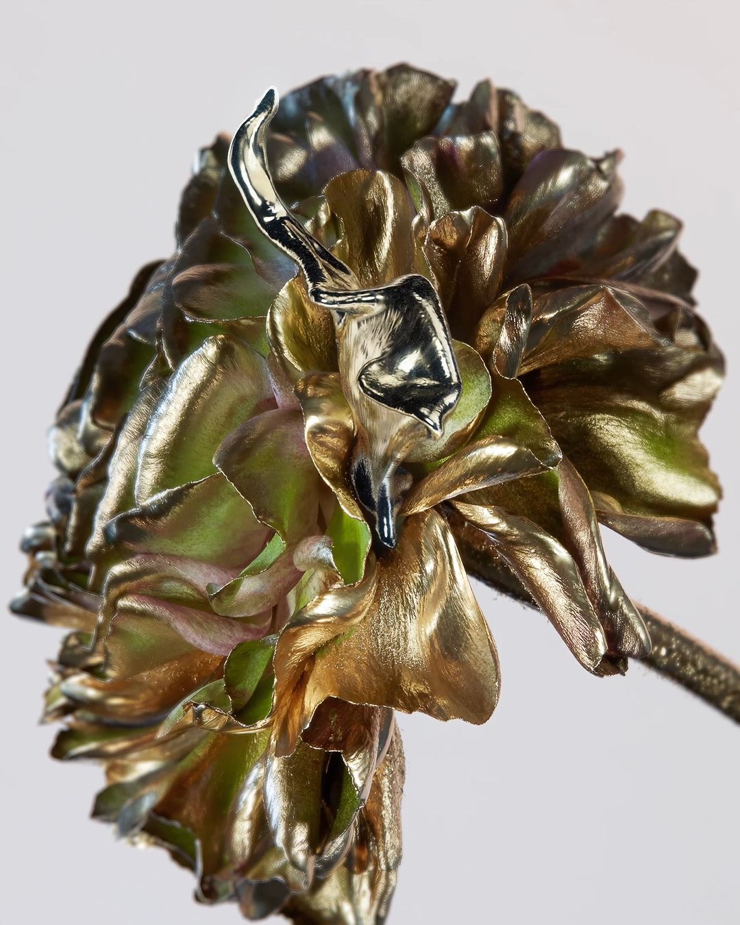 Close-up of a metal artichoke flower sculpture with gold and silver plating, showcasing a decorative and botanical art piece against a plain background.