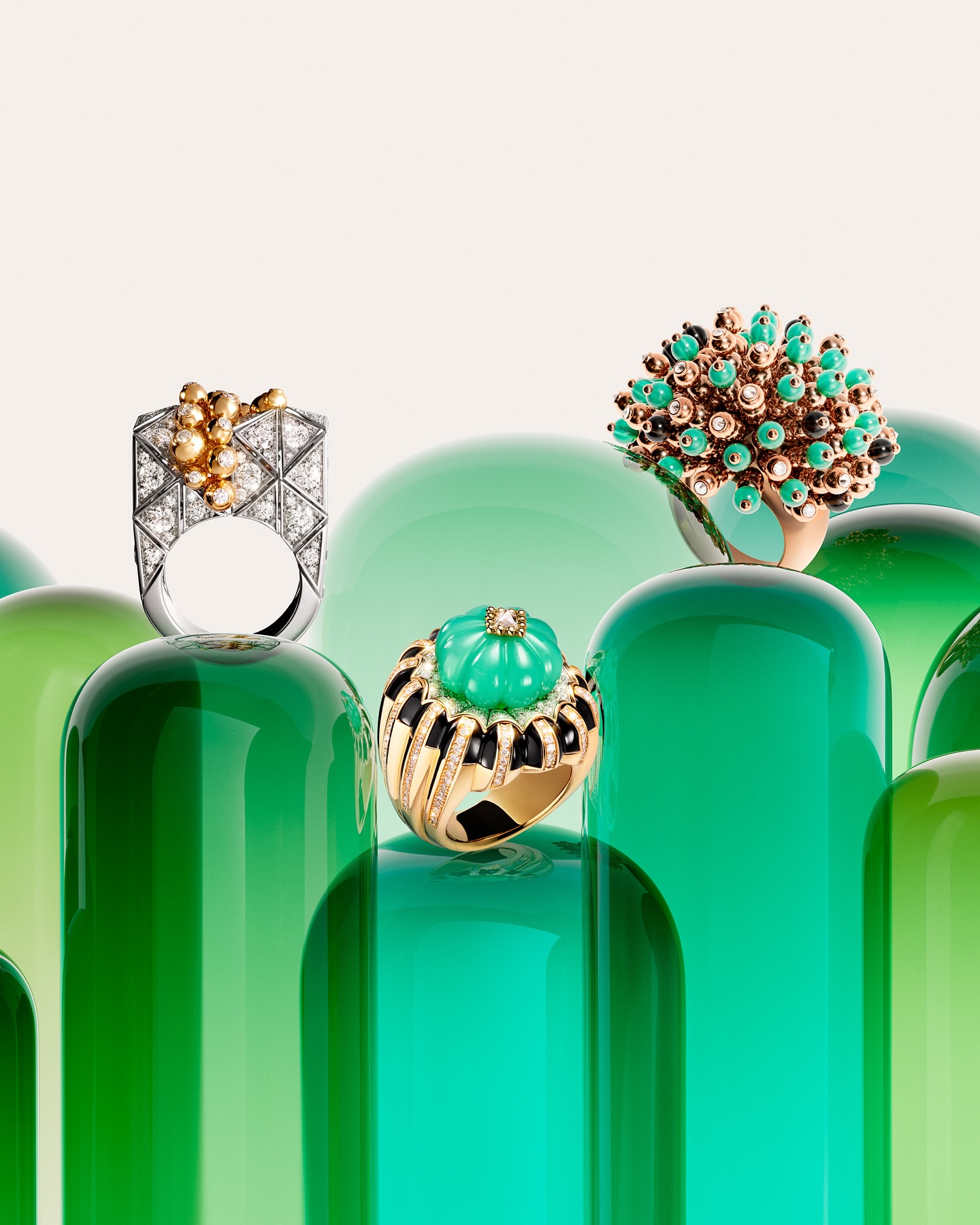 Close-up product shot of four ornate gold and gemstone rings arranged on glossy green pedestals against a gradient white backdrop.