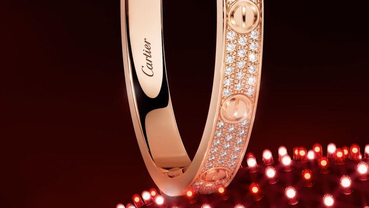 Elegant Cartier bracelet with diamonds on a reflective red surface, close-up studio shot showcasing luxury jewelry and brand detail.
