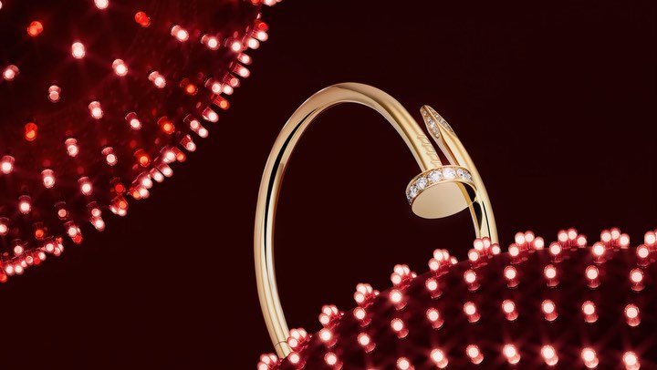 Close-up of a gold nail-style bangle with diamond accents, set against a deep red background dotted with tiny glowing red lights.