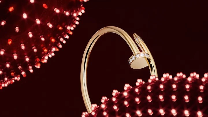 Close-up of a gold nail-style bangle with diamond accents, set against a deep red background dotted with tiny glowing red lights.