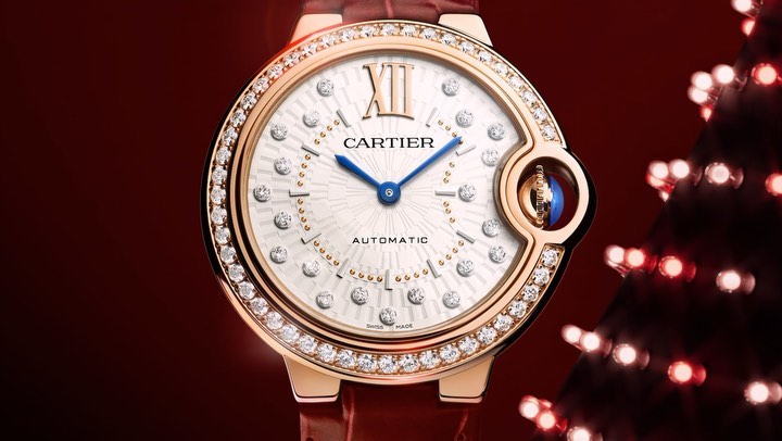 Close-up of a gold Cartier watch with diamond bezel, set against a deep red background with bokeh lights; luxury time piece detail.