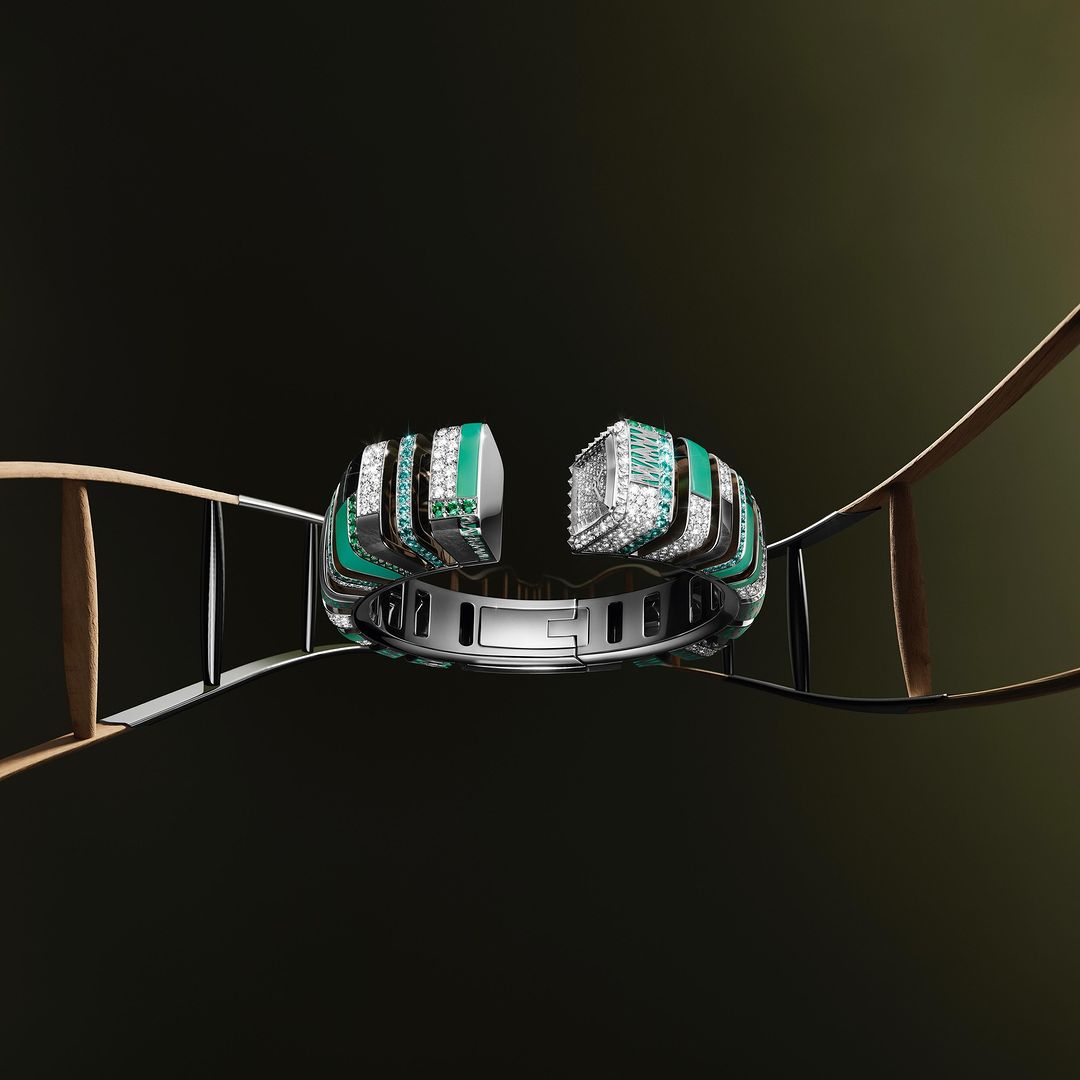 Close-up of a silver cuff bracelet with green and diamond accents, presented on a thin ladder against a dark background.