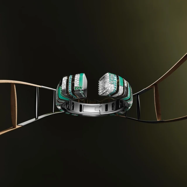 Close-up of a silver cuff bracelet with green and diamond accents, presented on a thin ladder against a dark background.
