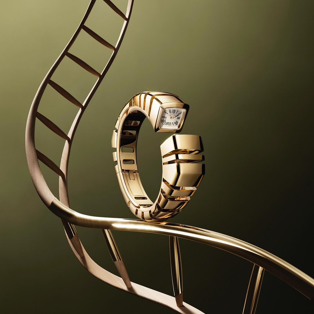 Elegant gold Bulgari Serpenti watch displayed on a stylized gold metal framework against a dark olive green background in studio lighting.