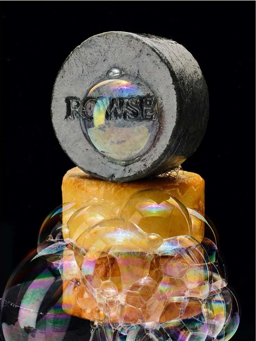 Stacked image features a gray concrete block with the word 'ROWSE' on it, sitting atop a block of soap surrounded by iridescent bubbles.