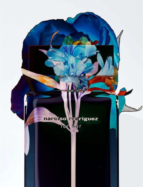 Artistic product shot of a black perfume bottle with blue and white floral accents, and the words 'NARCISO RODRIGUEZ for her' printed on it.