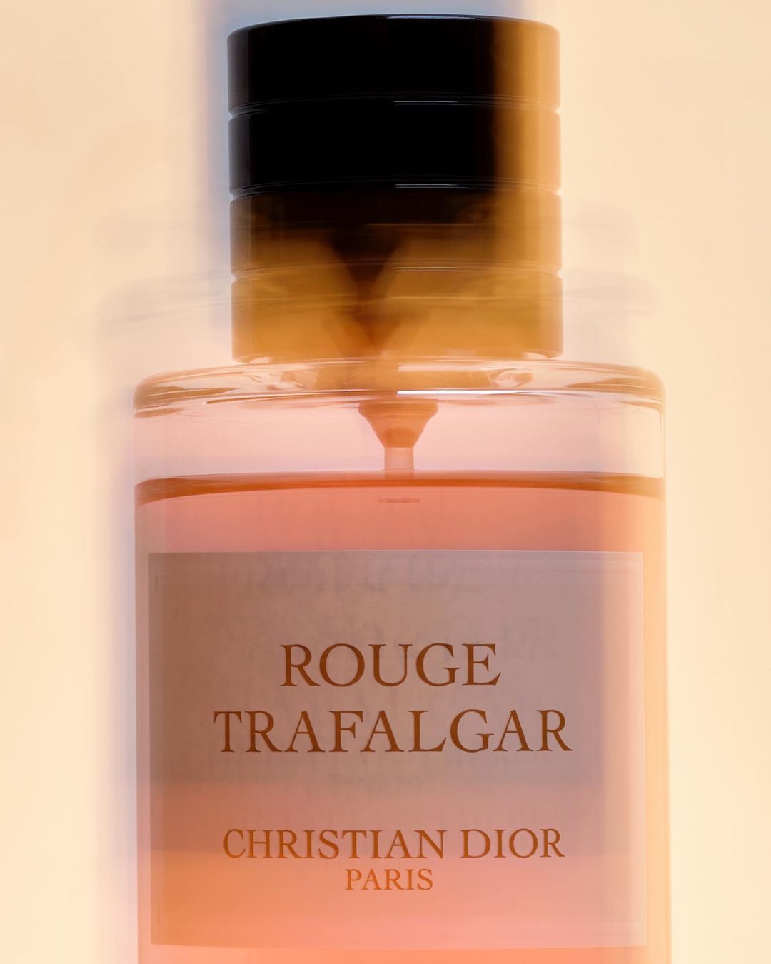 Close-up studio shot of a Christian Dior 'Rouge Trafalgar' fragrance bottle with a red liquid and black cap against a light background.