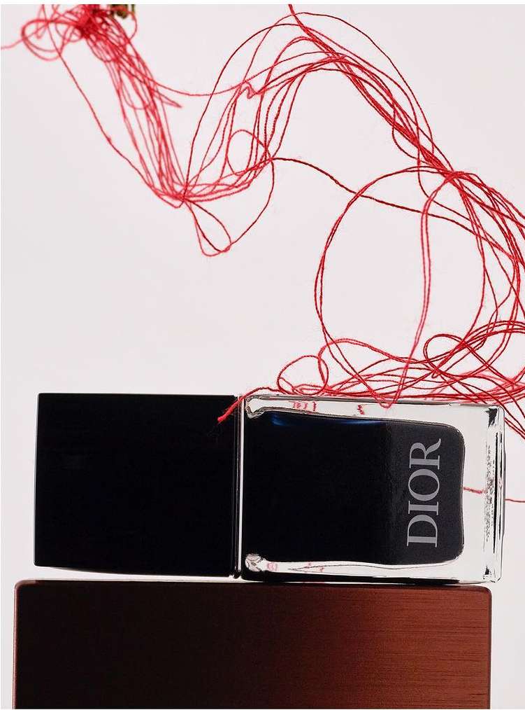 Close-up product shot featuring a Dior fragrance bottle with a black cap, set on a bronze base, and complemented by artful red string.
