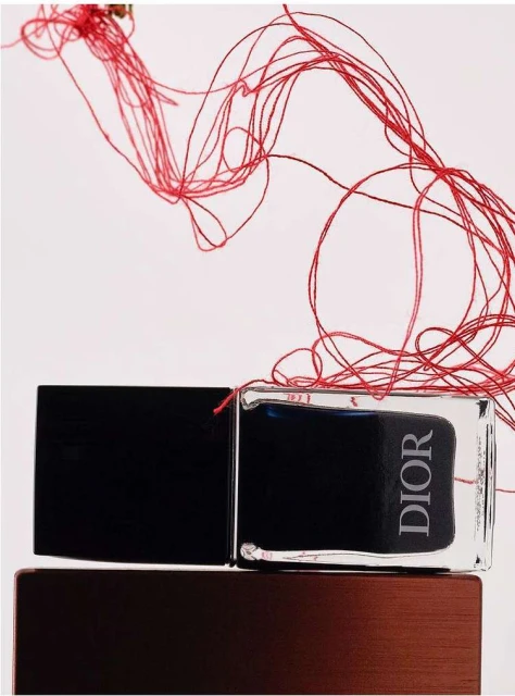 Close-up product shot featuring a Dior fragrance bottle with a black cap, set on a bronze base, and complemented by artful red string.