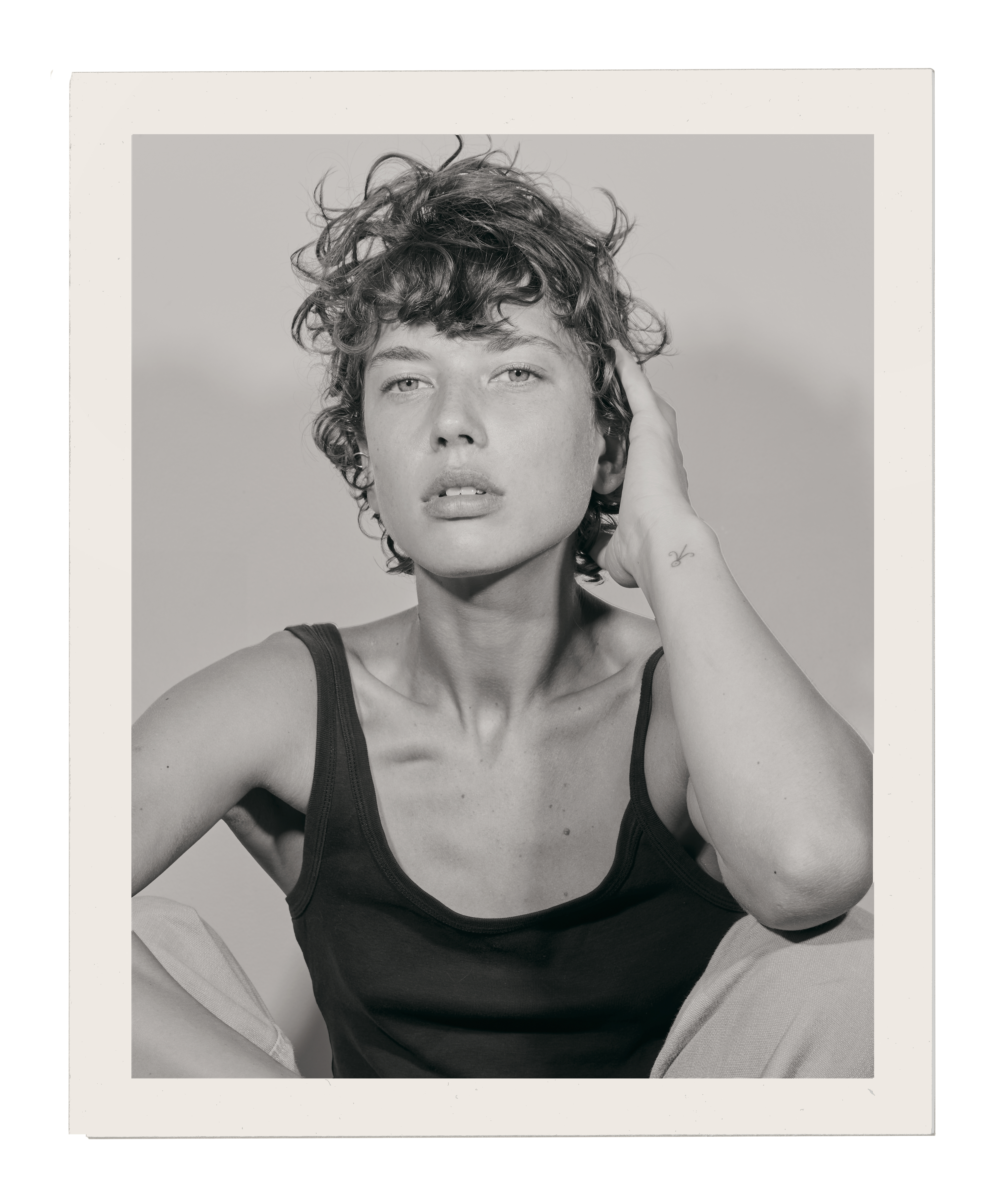 Monochrome portrait of a young woman with curly hair, wearing a tank top, and posing in a photo studio with neutral background.