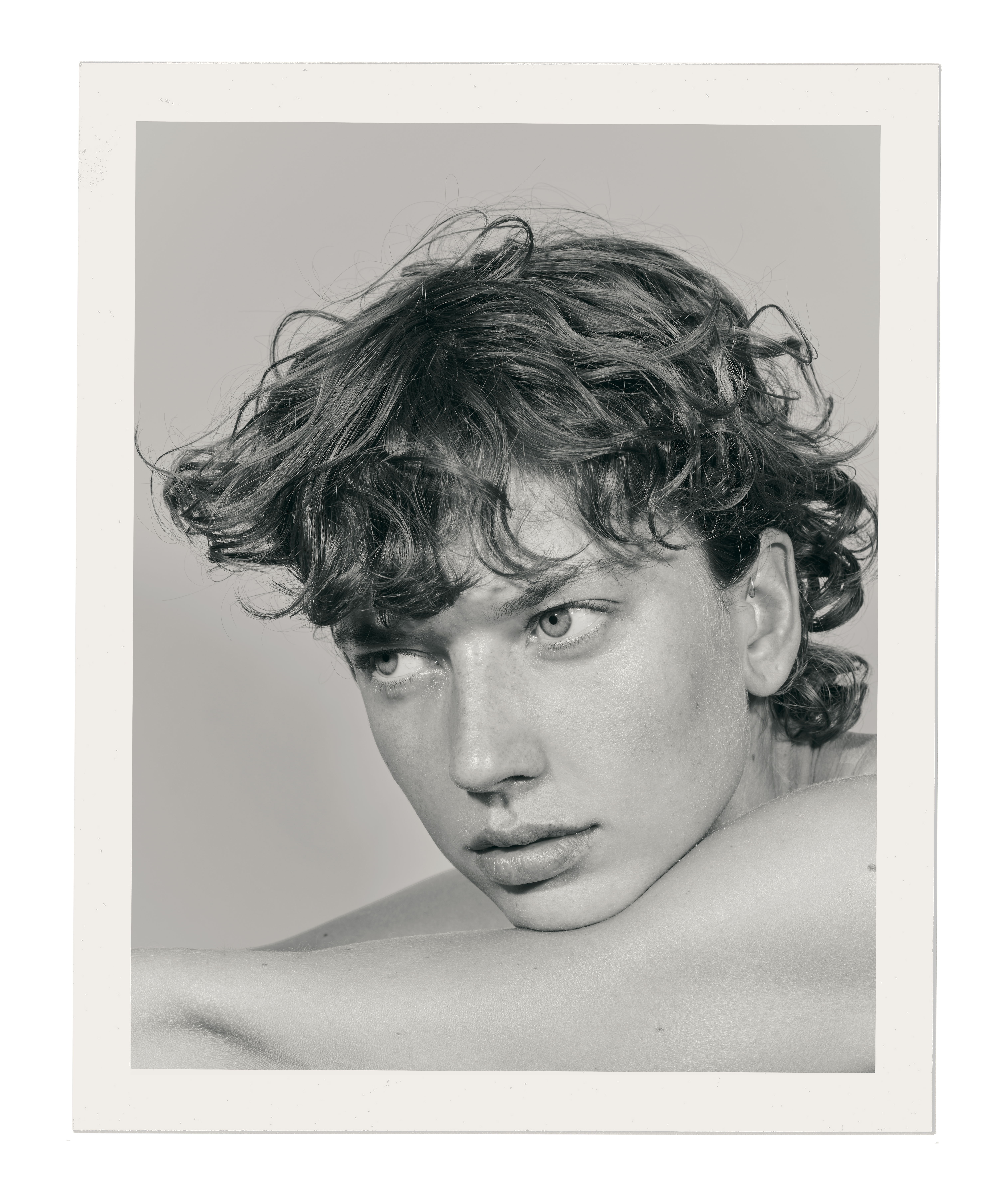 Monochrome portrait of a young adult male with curly hair and light eyes in a close-up studio shot, looking off-center.