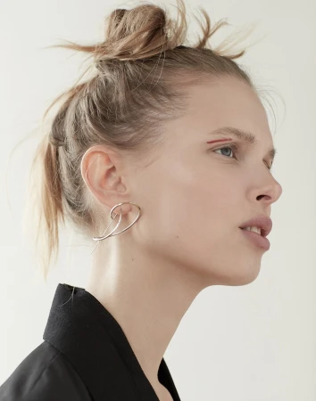 Close-up portrait of a woman wearing an abstract silver earring and a black top against a seamless white background.