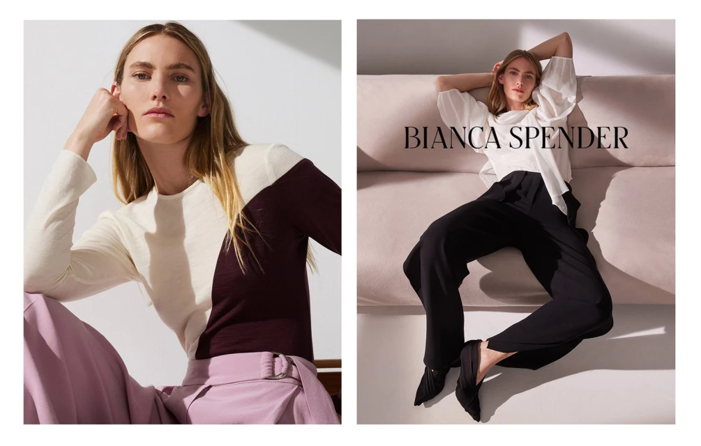 Fashion shot featuring a Caucasian female model wearing stylish pants and a long-sleeve top, posing indoors on a couch with soft lighting.