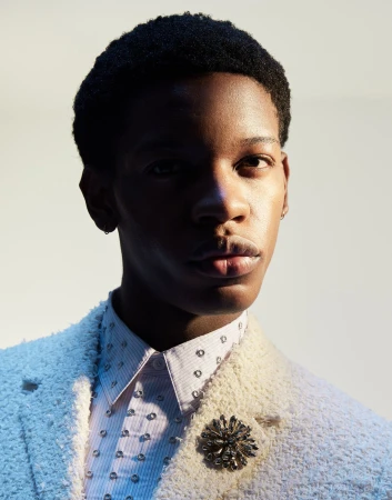 Portrait of a Black man wearing a textured white jacket and jeweled brooch by Manolo Campion