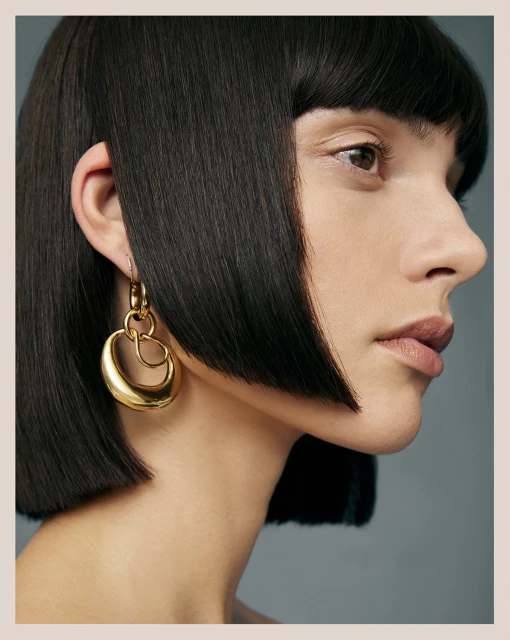 Close-up studio shot of a woman with dark bob hairstyle wearing gold loop earrings, showcasing beauty and fashion jewelry trends.