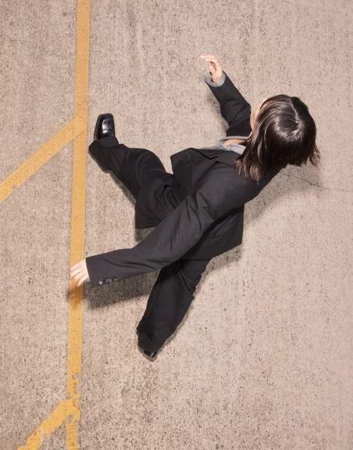 Overhead shot of a person in a business suit walking on a concrete surface marked with yellow lines, captured in natural light.