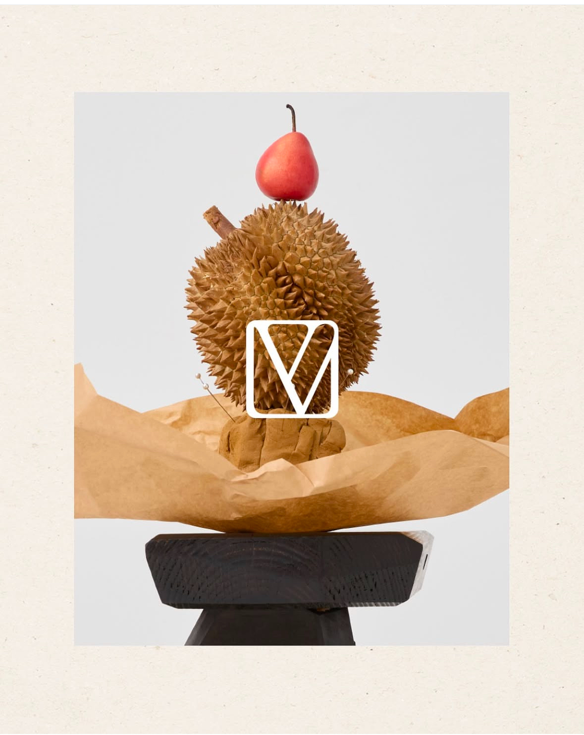 Still life of durian fruit topped with a pear, resting on a black wooden block and brown paper, set against a white background.