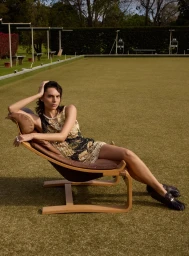 Woman in a beaded patterned dress relaxing in a wooden lounge chair on a bowling green in Sydney by Manolo Campion
