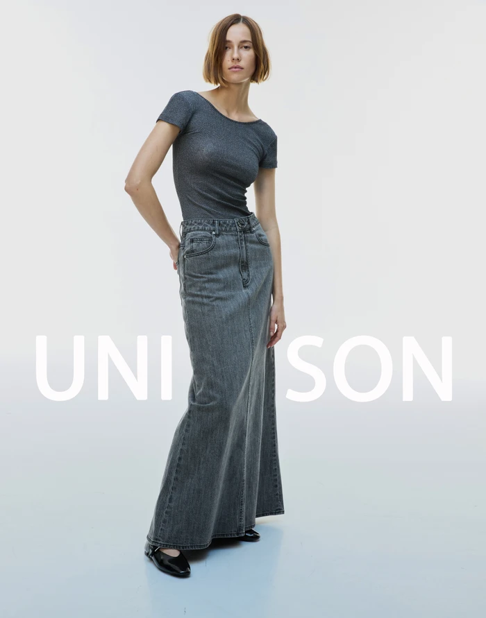 Model wearing a grey ribbed top and long denim skirt against a seamless white background, photographed by Manolo Campion